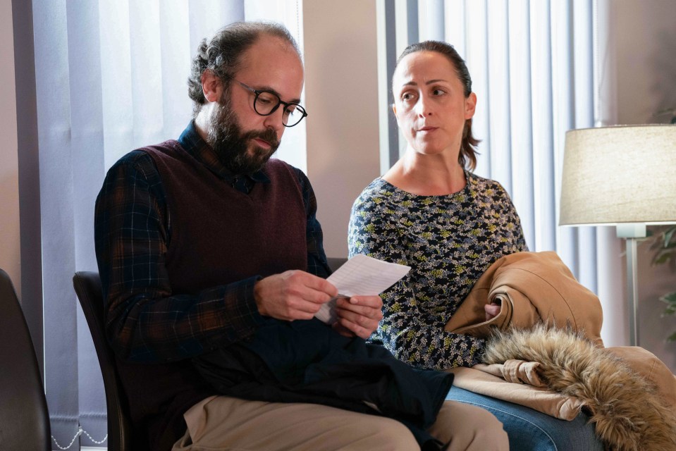 A man and woman sit in a waiting room, the man reading a piece of paper.