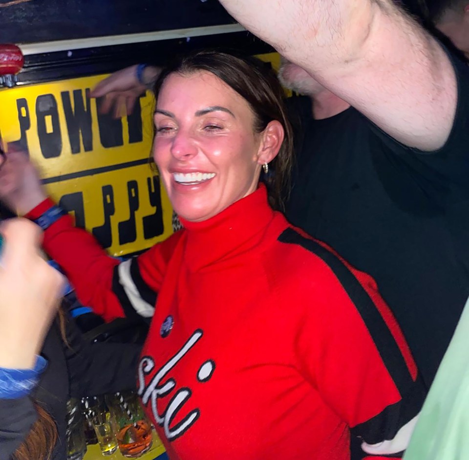 Coleen Rooney at a bar, wearing a red ski sweater.