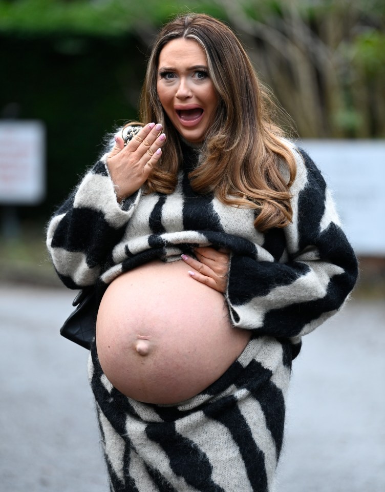 A pregnant woman in a black and white striped sweater looks surprised.