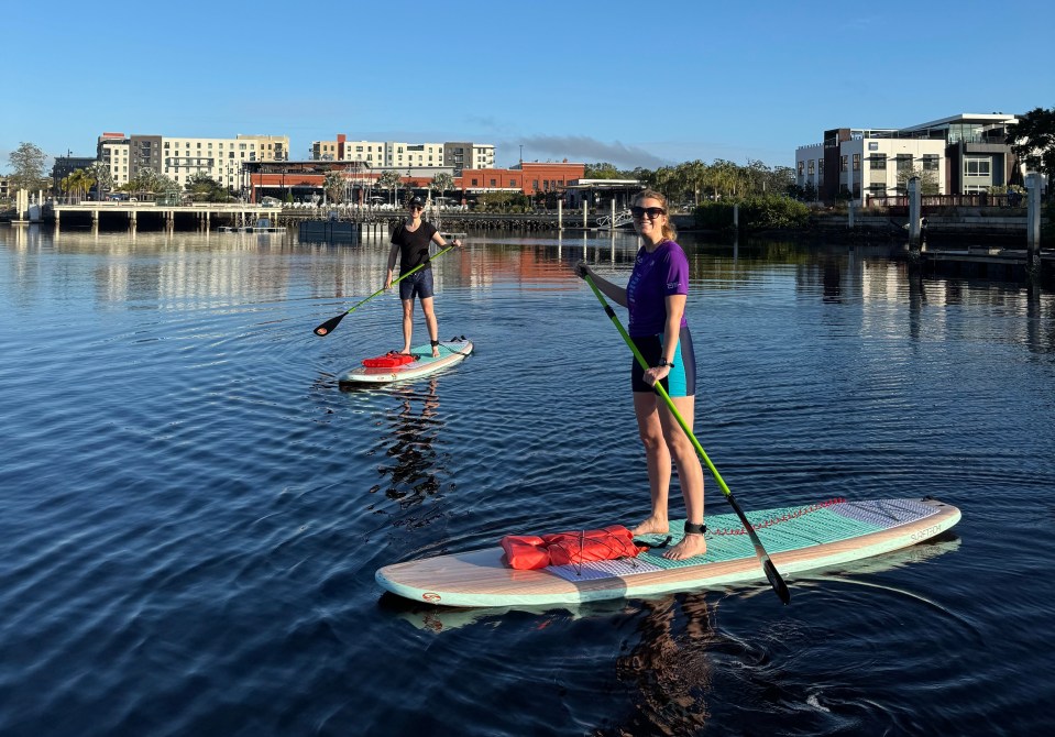 Two people paddleboarding on calm water in front of a city skyline.