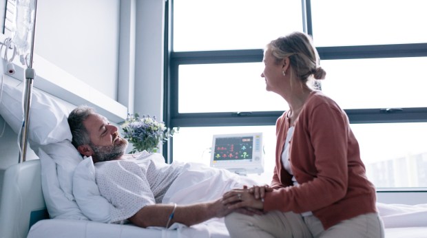 Wife holding her hospitalized husband's hand.