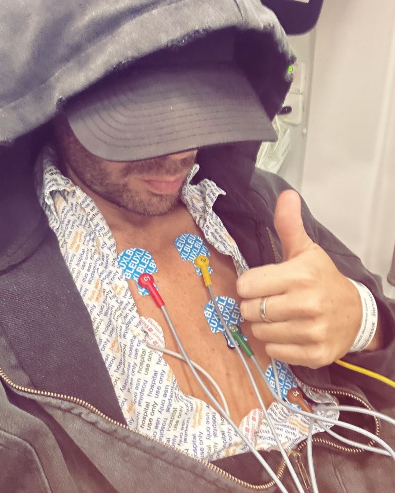 Man with heart monitor leads attached to his chest gives thumbs up.