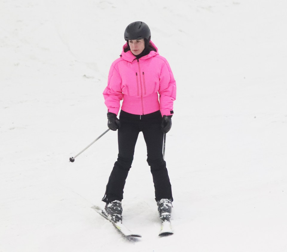 Woman in pink ski jacket and black pants skiing.