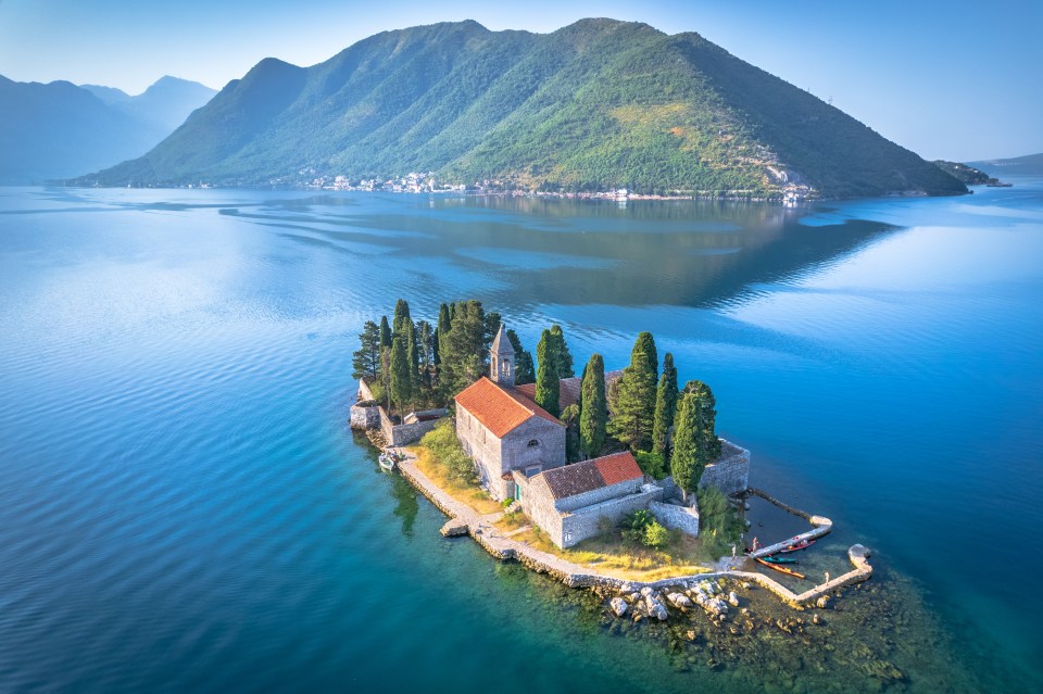 Aerial view of Our Lady of the Rocks island in Montenegro, featuring a church and surrounding buildings.