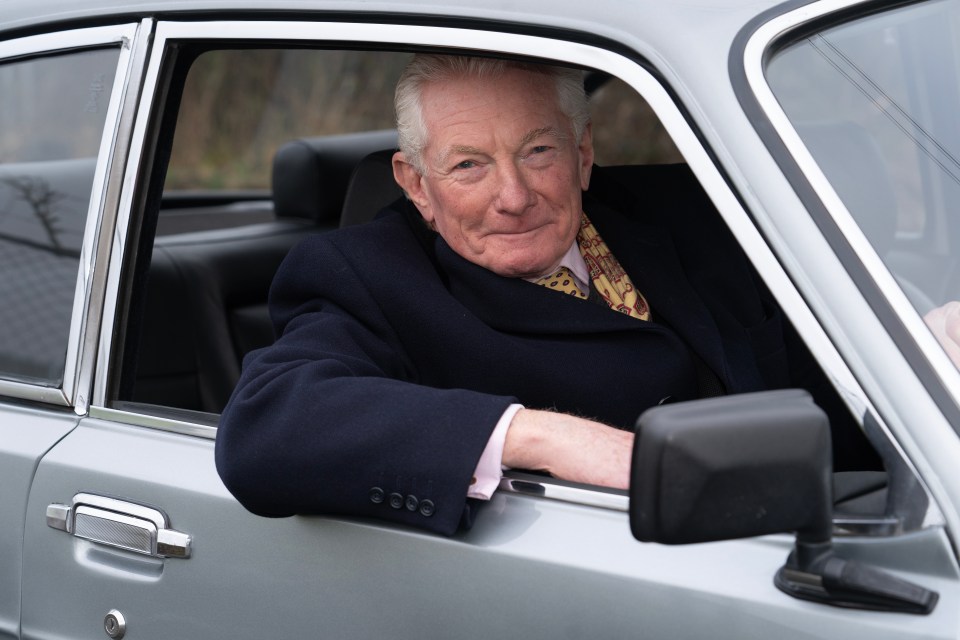 Older man sitting in a silver Bristol Brigand classic car.