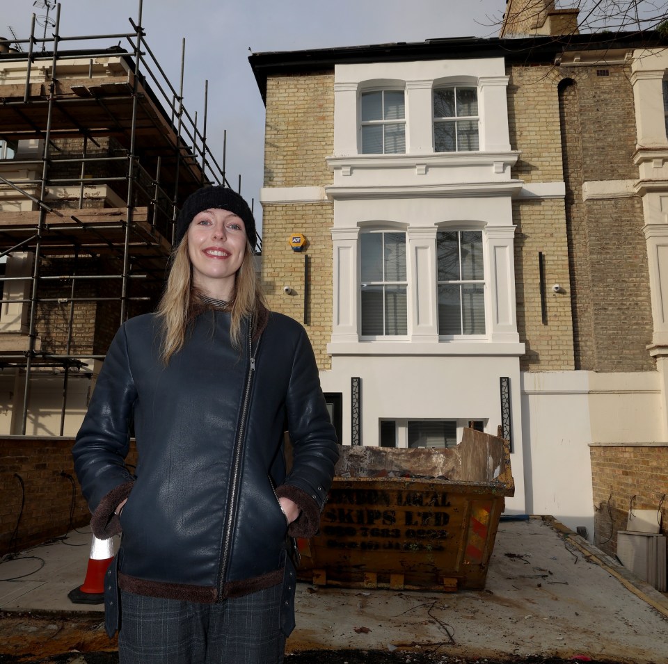 A woman stands in front of a house under construction.