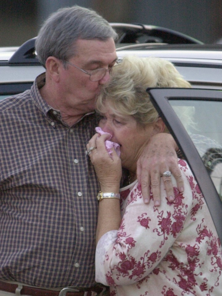 A grieving woman is comforted by her husband.