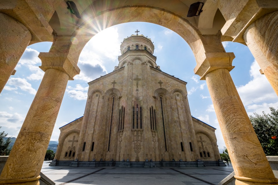 The Holy Trinity Cathedral of Tbilisi, Georgia, viewed through a stone archway.