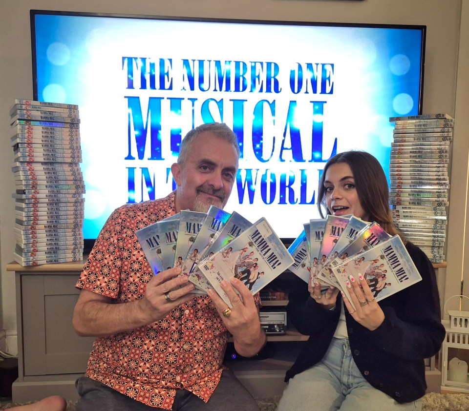 A woman and man holding multiple copies of the Mamma Mia! DVD.