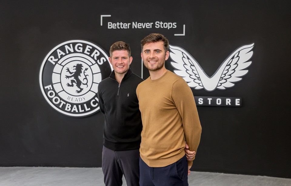 Two men stand in front of a Rangers Football Club store sign.