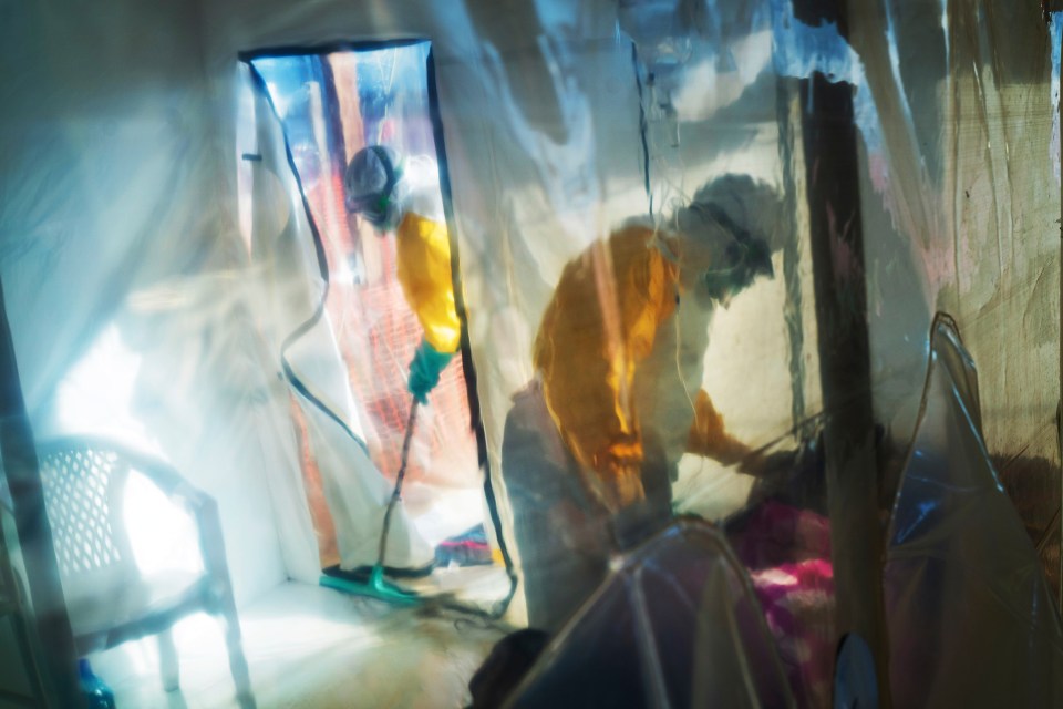 Health workers in protective suits tending to an Ebola victim in an isolation tent.