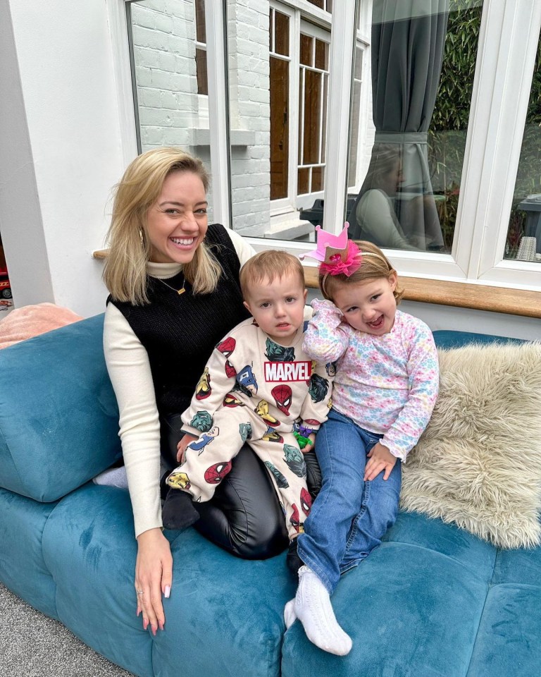 A woman sits on a teal couch with her two young children.