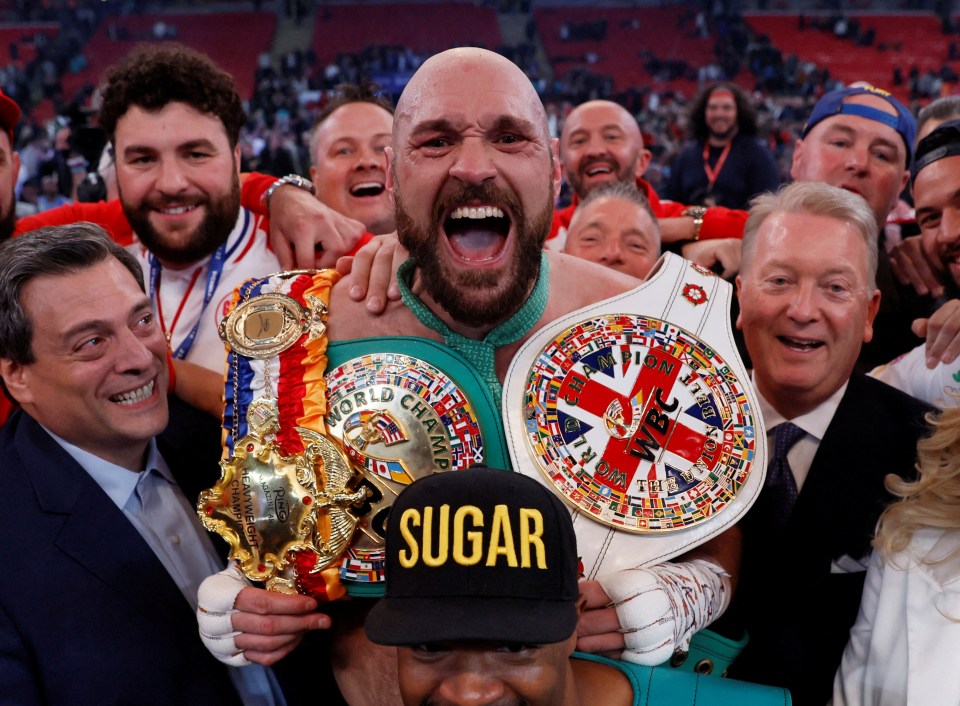 Tyson Fury celebrates a boxing victory with championship belts.