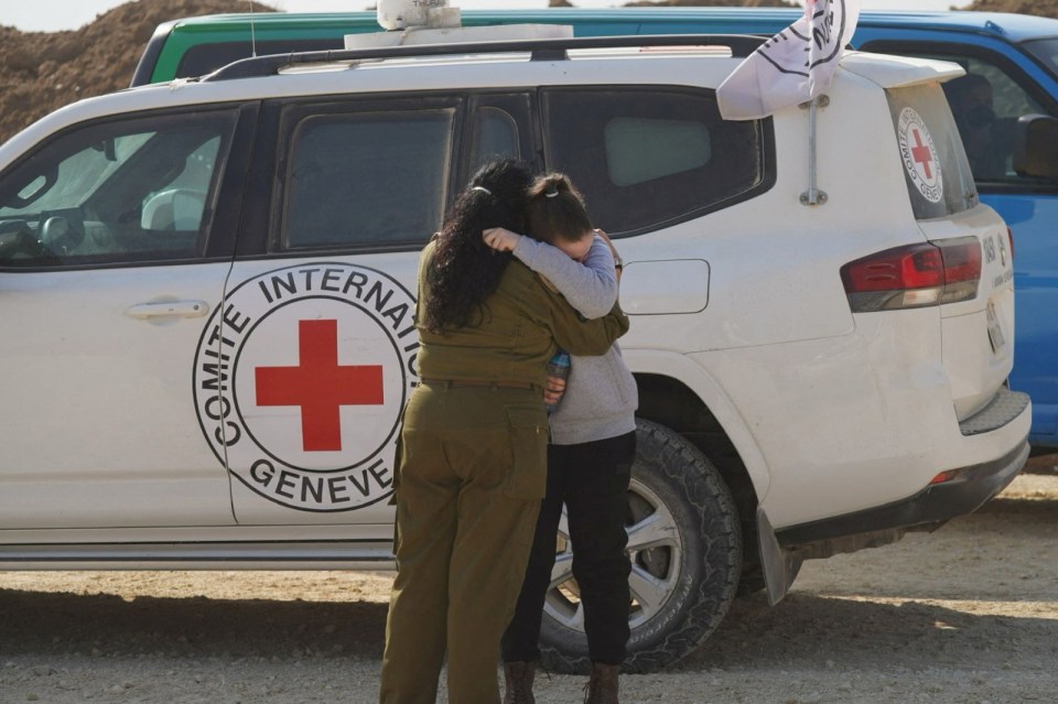 A released Israeli hostage embraces an Israeli military officer near a Red Cross vehicle.