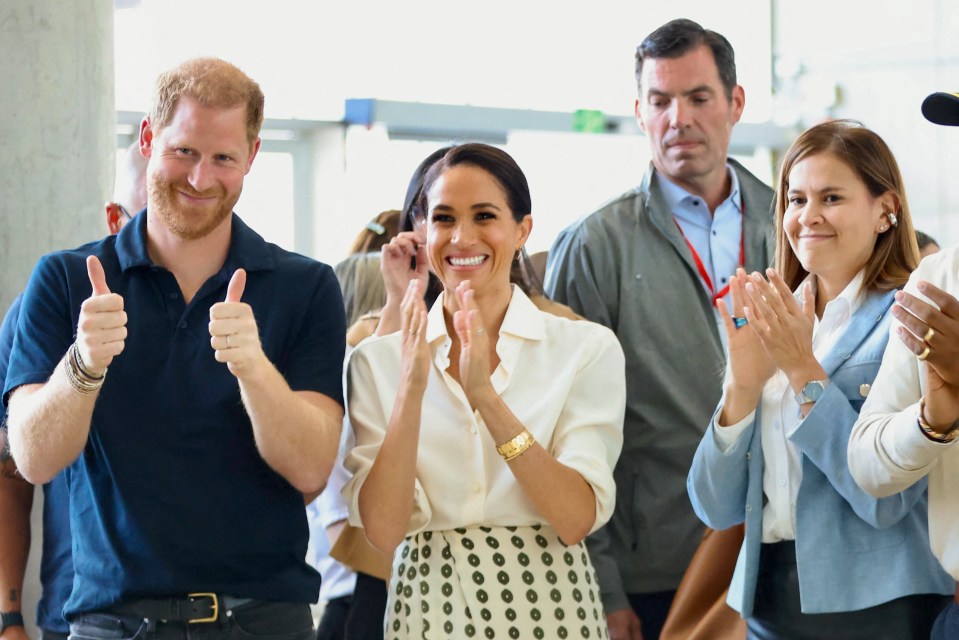 Prince Harry and Meghan Markle giving thumbs up and clapping.