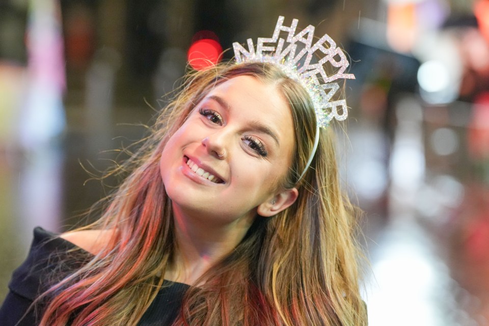 A cheerful partygoer beams while wearing a 'Happy New Year' hairband