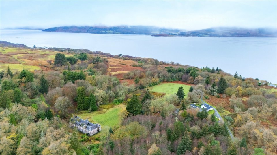 Aerial view of a derelict nine-bedroom mansion on a wooded peninsula.