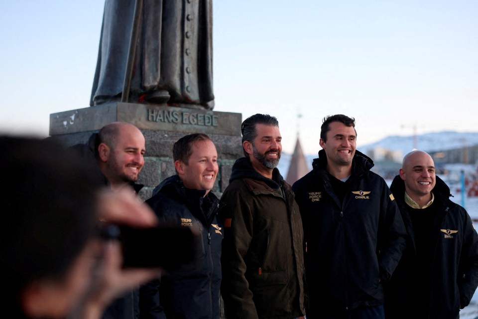 Donald Trump Jr. and several men in Trump Force One jackets stand in front of a statue in Nuuk, Greenland.