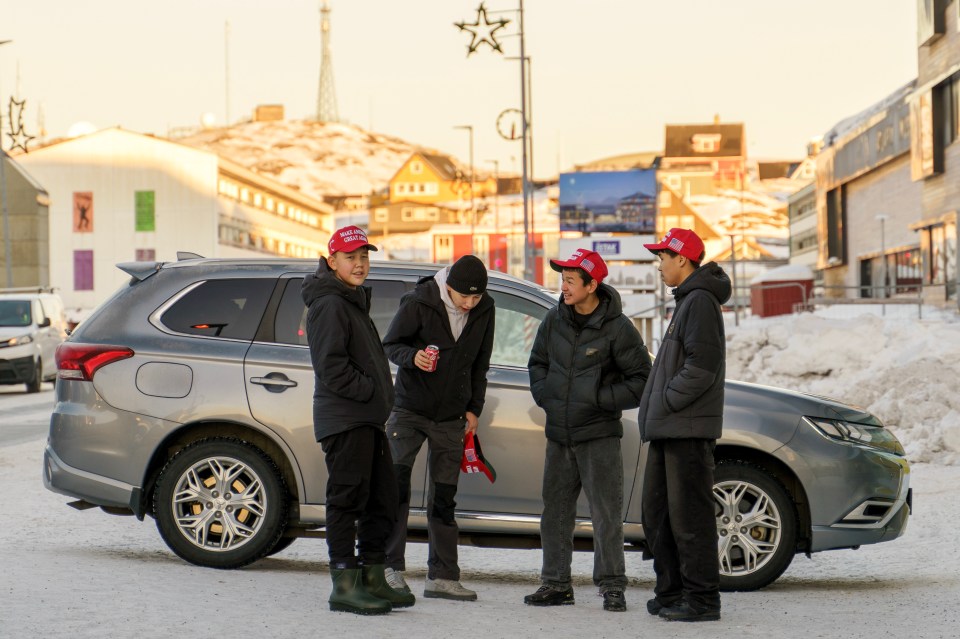 Four young people wearing "Make America Great Again" hats stand by a car in Greenland.