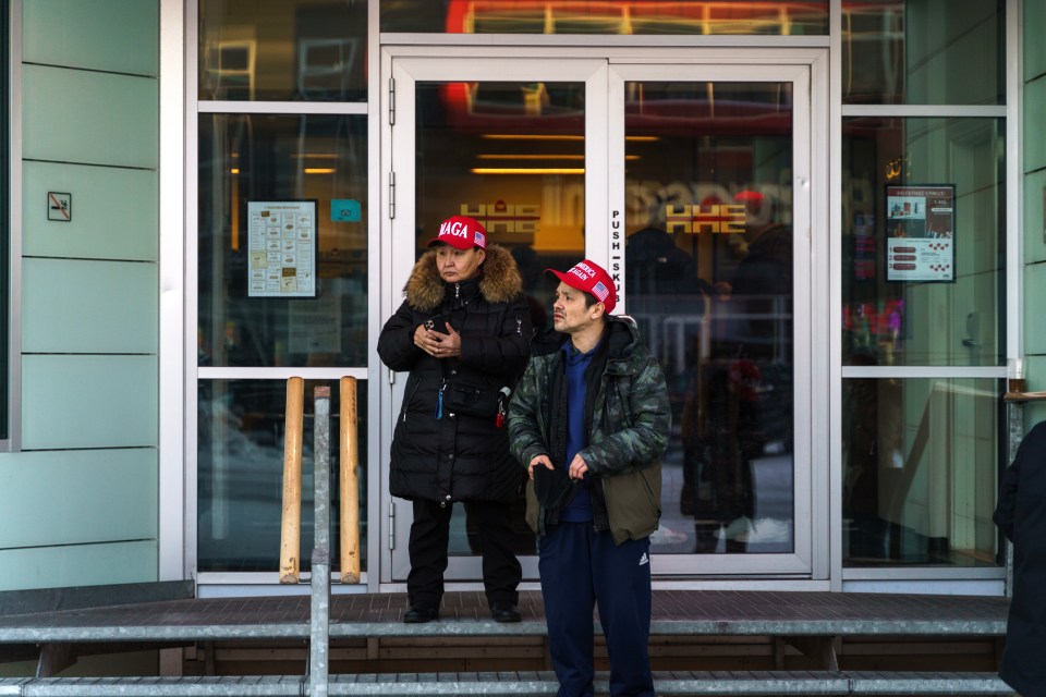 Two people wearing MAGA hats stand outside a building in Greenland.