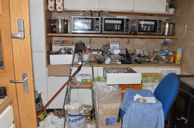 A cluttered office with shelves full of various items and a chair.