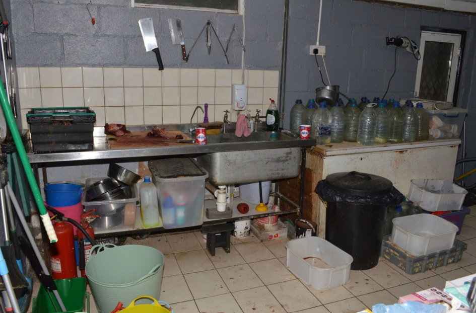 Bloody butcher's shop workspace with various containers and cleaning supplies.