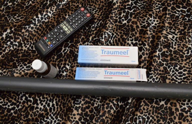 Two tubes of Traumeel ointment, a remote, and a small bottle on a leopard-print fabric.