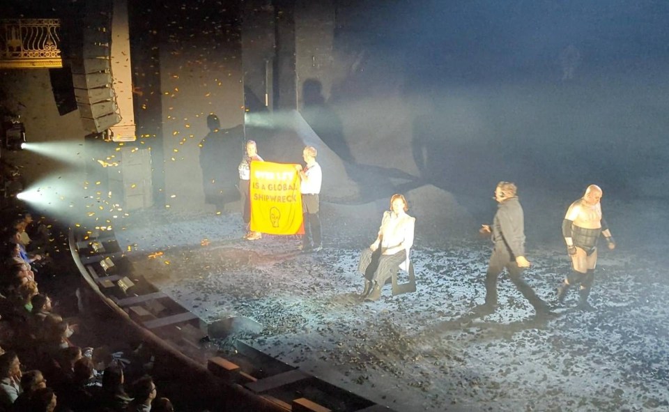 Protesters on stage during a West End performance of The Tempest holding a sign that reads "Over 1.5 degrees is a global shipwreck".