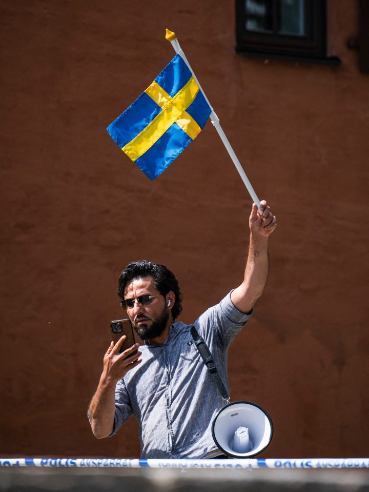 Man holding a Swedish flag and megaphone, using a phone.