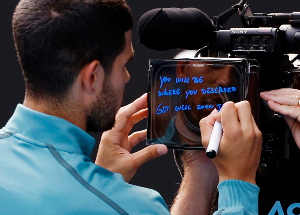 Carlos Alcaraz writing "You will be where you deserved. Get well soon J" on a TV camera.