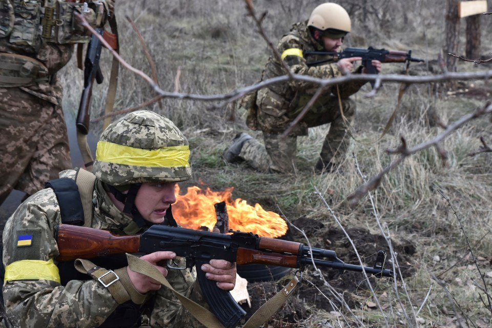 Ukrainian servicemen training with rifles near a fire.