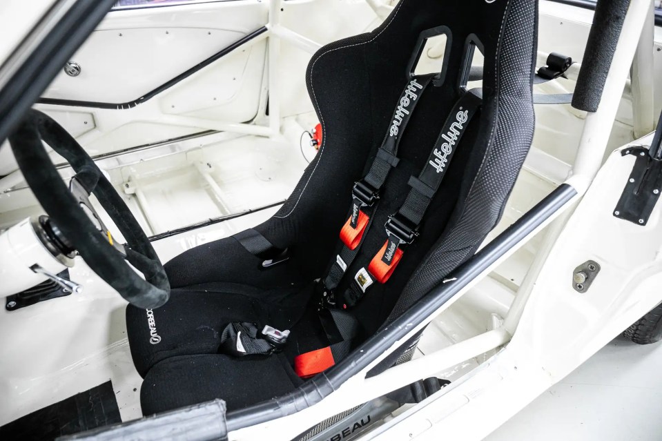 Interior of a white 1966 Ford Mustang race car, showing the driver's seat and safety harness.