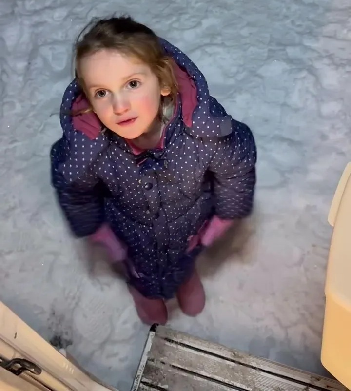 Young girl in winter coat standing in the snow.