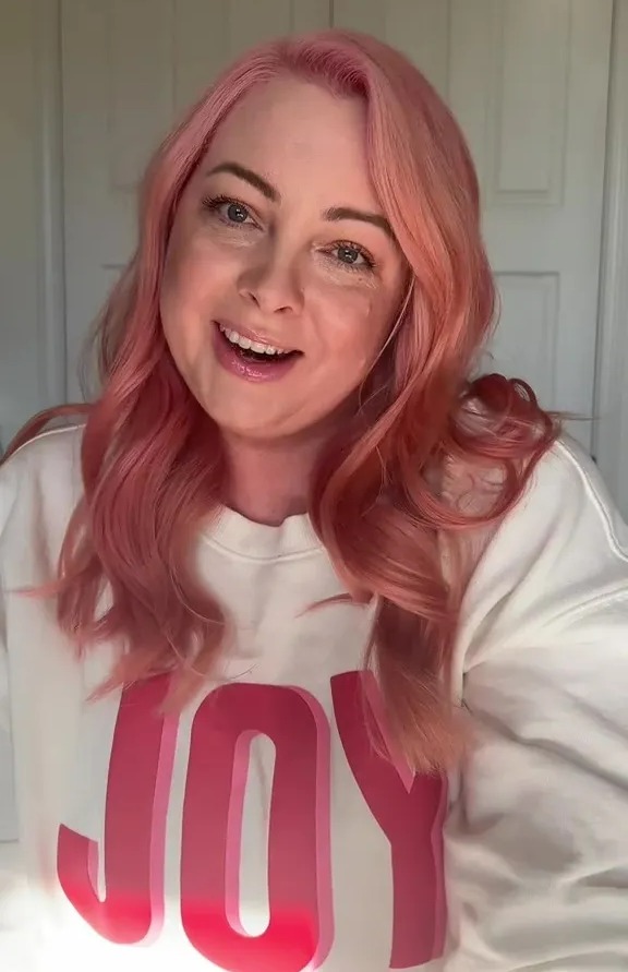 Woman with pink hair wearing a sweatshirt that says "JOY".