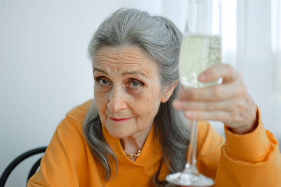 Older woman with gray hair raises a glass of champagne.