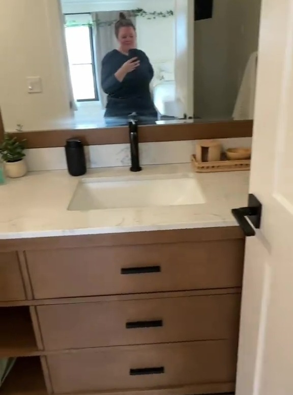 Bathroom vanity with a mirror reflecting a woman.