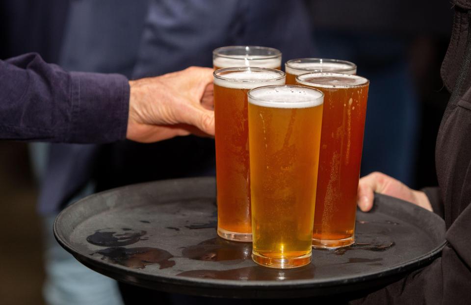 Person selecting a glass of beer from a tray of beers.