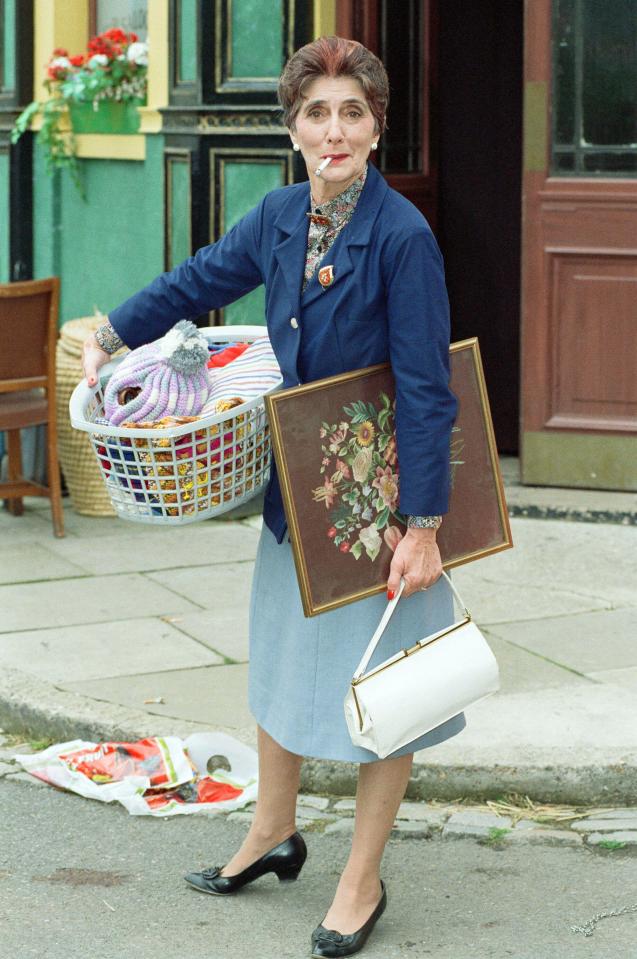 June Brown as Dot Cotton on the set of EastEnders, carrying a laundry basket and a framed picture.