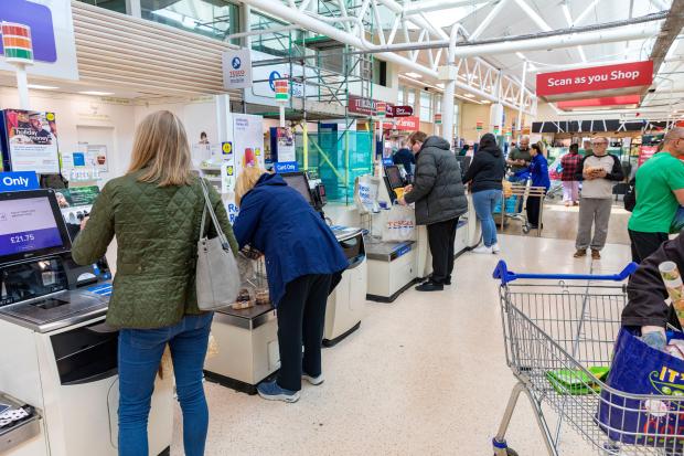 Tesco supermarket customers using self-checkout kiosks.