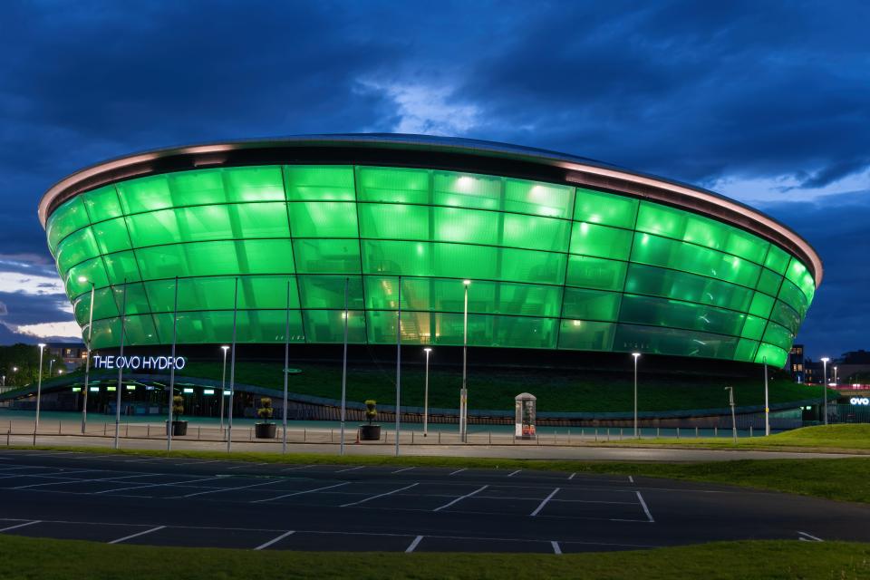 The OVO Hydro arena in Glasgow at night, illuminated in green.