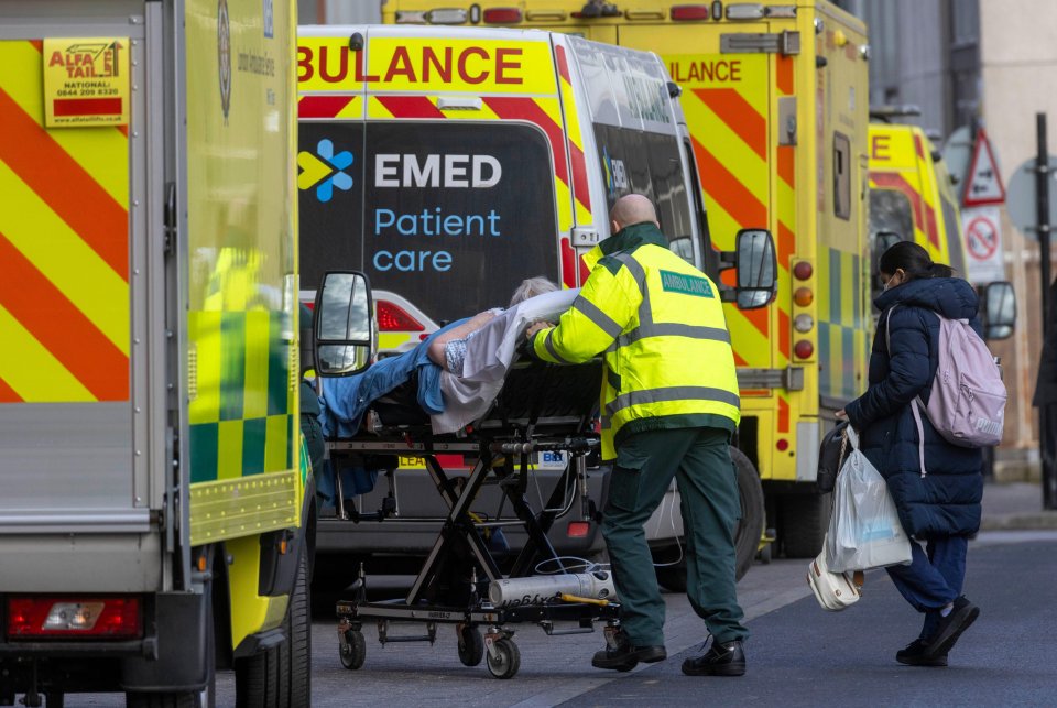 Paramedic pushing a patient on a stretcher past ambulances.