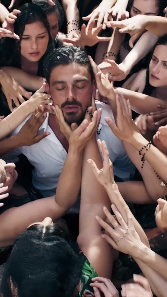 Michele Morrone surrounded by women's hands in a Dolce & Gabbana ad.