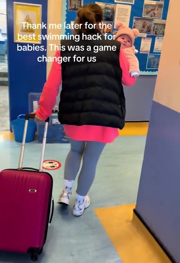 Woman carrying baby in a baby carrier while pulling a suitcase.