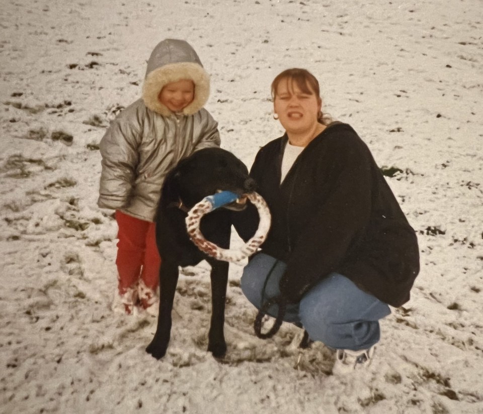 A woman and young child playing with a dog in the snow.