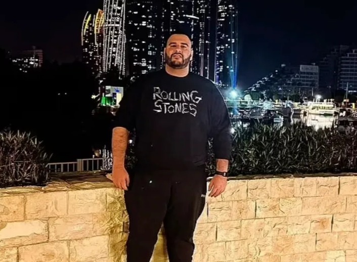 Man in Rolling Stones sweatshirt standing in front of city skyline at night.