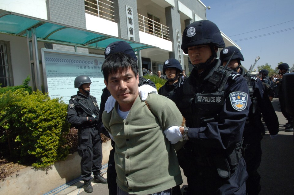 A handcuffed man escorted by Chinese police officers.