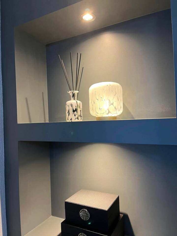 A built-in shelf with a lamp, reed diffuser, and boxes.