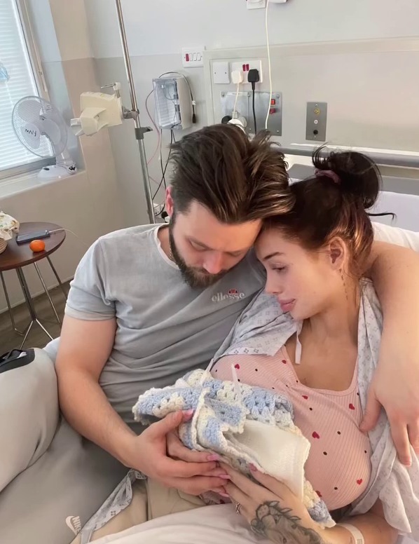 Parents holding their deceased newborn baby in a hospital bed.