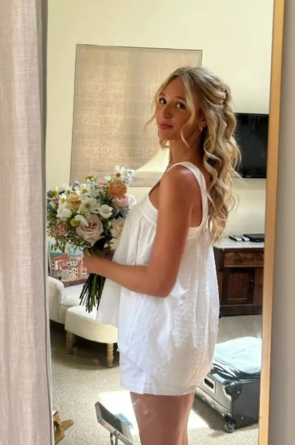 Bride in white pajamas holding wedding bouquet.