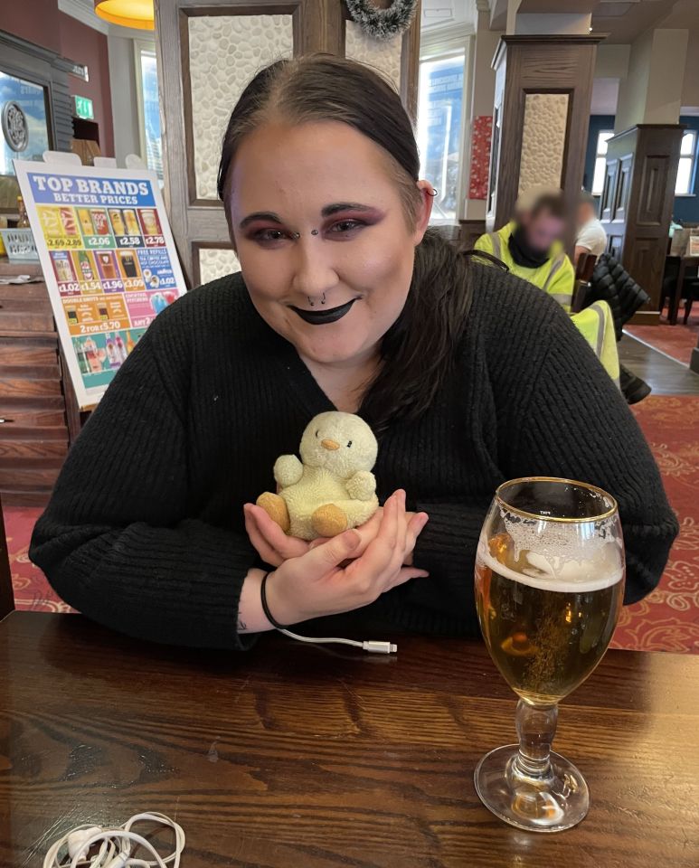 Woman holding a small stuffed chick, with a pint of beer on the table.